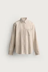Camisa de corte regular fit confeccionada en una mezcla de lino y algodón, color beige. Presenta cuello abotonado, manga larga con puños abotonados, un bolsillo de parche en el pecho y cierre frontal con botones.