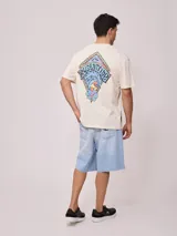 Remera holgada de algodón color beige, de manga corta y cuello redondo, con un gran estampado colorido en la espalda con diseño de olas y la inscripción 'Rusty Tribe'.