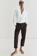 Pantalón chino de tiro bajo color marrón oscuro, con pernera recta y bajo con vuelta. Incluye un cinturón trenzado delgado de color marrón claro. Cuenta con bolsillos delanteros y cierre frontal con cremallera y botón.