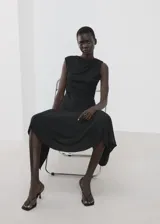 Vestido midi negro con diseño asimétrico, cuello redondo drapeado y detalle de frunces en el lateral. Falda de corte evasé con terminación en puntas.