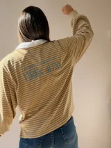 Buzo tipo chomba de corte oversize con diseño a rayas horizontales celestes y blancas. Presenta cuello camisero blanco y un bordado en la espalda con la inscripción República Oriental del Uruguay.
