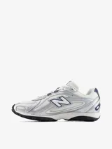 Championes New Balance modelo U204LPC, de estilo inspirados en el running de los años 2000, con capellada de malla blanca y superposiciones metalizadas plateadas con detalles en azul marino.