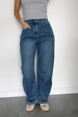 Pantalón de jean con corte balloon fit, de tiro alto y diseño holgado en las piernas. Confeccionado en denim con elastano, presenta un lavado azul clásico y cierre frontal con botón y cremallera.