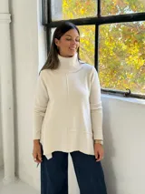 Sweater de punto color beige con cuello alto tipo polera, diseño holgado y costuras visibles en el frente.