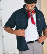 Camisa de manga corta color azul marino de corte boxy, con cuello inglés, cierre frontal de botones metálicos a presión y bolsillos cargo en el pecho.