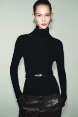 Jersey de punto liso confeccionado en 100% lana, con cuello subido y manga larga. Incluye un cinturón fino integrado en la cintura con hebilla metálica.