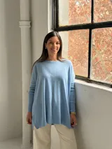 Sweater de punto color celeste, con cuello redondo, corte holgado y mangas largas con puños acanalados. Presenta un detalle de costura vertical central en el frente.