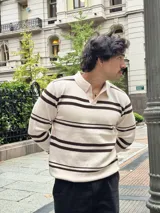 Buzo tejido de punto con diseño a rayas horizontales en color beige y marrón. Presenta cuello tipo polo con cierre frontal parcial y puños acanalados.