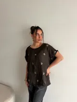 Blusa de símil gamuza color marrón oscuro, de corte holgado, mangas cortas y escote redondo, adornada con sutiles bordados florales distribuidos en la prenda.