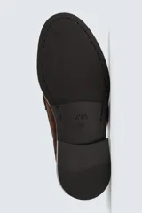 Mocasín de vestir para hombre, color marrón oscuro, fabricado en piel con acabado serraje (gamuza). Presenta un antifaz en el empeine con costuras visibles y suela a contraste con ligero tacón.