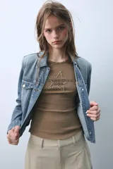 Musculosa de algodón con cuello redondo y diseño sin mangas. Presenta un estampado frontal con el texto Arizona Est. 1975 y detalle de tachas metálicas decorativas en el escote y las sisas.