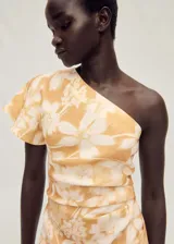Vestido midi de lino con estampado floral en tonos amarillos y blancos. Presenta un diseño asimétrico con un solo hombro, cintura drapeada y una abertura lateral en el bajo.