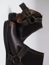 Bota de cuero color marrón oscuro con punta cuadrada, diseño tipo chelsea con paneles elásticos laterales y estribo decorativo con hebilla metálica ajustable.