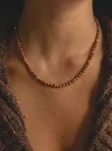 Collar corto de piedras esféricas color marrón brillante con destellos dorados, intercaladas con pequeñas cuentas metálicas doradas.