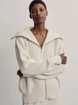 Campera larga tejida color crema con cierre frontal, cuello alto y diseño texturizado.