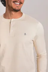 Remera de manga larga tipo Henley, color beige, con cuello redondo y tapeta con botones. Presenta un pequeño logo bordado en el pecho.