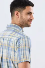 Camisa sport de manga corta con estampa a cuadros en tonos celestes, amarillos y blancos, con cuello camisero abotonado y bolsillo frontal en el pecho.