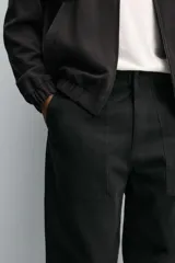 Pantalón de corte recto confeccionado en tejido de algodón con estructura diagonal. Presenta cintura ajustable en los laterales con trabillas, bolsillos delanteros tipo cargo y bolsillos traseros con solapa. Cierre frontal con cremallera y botón.