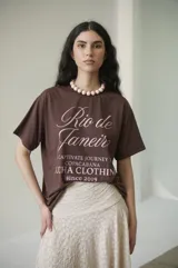 Remera de algodón blanca con estampado frontal en negro que dice "Rio de Janeiro" en letra cursiva y "Captivate Journey to Copacabana Lucha Clothing since 2019".