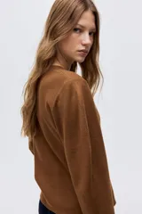 Cárdigan de punto color marrón, con cuello en V y cierre frontal de cuatro botones oscuros. Presenta un calce holgado y mangas largas.