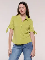 Camisa de corte entallado y tejido suave, color verde, con cuello solapa, escote en V y cierre frontal con botones. Presenta detalles de bordado floral al tono sobre el canesú y mangas cortas con puño y lazo para anudar.