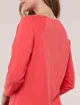 Remera blanca de algodón con elastano, de corte semi holgado, escote bote con ojalillos metálicos frontales, mangas tres cuartos raglán y ruedo asimétrico curvado.