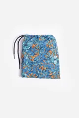 Short de baño celeste con estampado de hojas pequeñas en tonos verdes y blancos. Cuenta con cintura elástica con cordón ajustable, bolsillos laterales y un parche circular con logo en la parte inferior.
