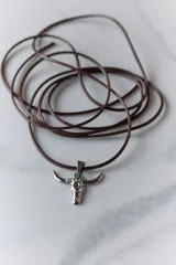 Collar con dije de acero quirúrgico en forma de cráneo de toro, montado sobre un cordón marrón.