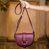 Bandolera morral color bordó, de material símil cuero, con solapa frontal, presilla y hebilla metálica plateada. Cuenta con correa larga regulable y cierre bajo tapa.