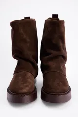 Bota de caña media confeccionada en cuero vacuno color marrón oscuro, con diseño de pliegues en la caña y suela de goma al tono con textura estriada.