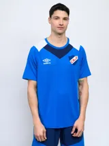 Remera de entrenamiento Umbro del Club Nacional de Football, color azul con detalles en blanco y azul marino en los hombros y cuello. Presenta el logo de la marca y el escudo del club en el pecho.
