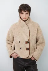 Chaqueta tipo gamulán de color marrón, con solapas amplias forradas en corderito sintético oscuro. Presenta un diseño cruzado con botones frontales y mangas largas, ideal para un estilo invernal.