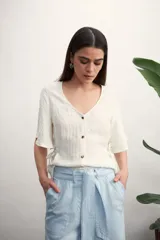 Camisa negra con botones dorados, escote en V y mangas cortas amplias con lazos laterales. 