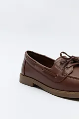 Zapato náutico de cuero sintético color marrón, con cordones decorativos, costuras a la vista y suela de goma antideslizante.