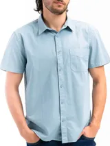 Camisa de manga corta color celeste claro, confeccionada en algodón, con cuello clásico y un bolsillo de parche en el lado izquierdo del pecho.