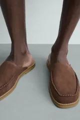 Zueco de piel con acabado serraje en color marrón, diseño sin talón, puntera redonda y detalle de costura tipo mocasín en el empeine.