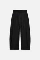 Pantalón negro de tiro alto y pernera ancha, confeccionado en tejido fluido, con bolsillos laterales y detalles de pliegues en la parte delantera.