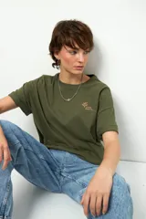 Remera de algodón color verde oliva, corte oversize, con mangas cortas dobladas y cuello redondo. Presenta un pequeño estampado en el pecho con un logo de hojas y el texto "LOVE EARTH".