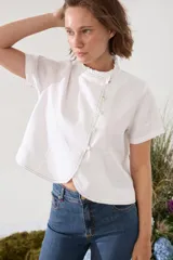 Blusa de lino verde de manga corta y corte recto, con cuello alto con volado y cierre frontal cruzado con botoncitos dorados.