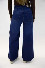 Pantalón jean de tiro alto y corte campana en color azul medio, con bolsillos delanteros y traseros, y cierre frontal con botón y cremallera.