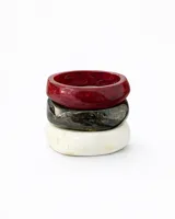 Set de tres brazaletes anchos y rígidos de resina con acabado brillante. Incluye uno color rojo oscuro veteado, uno negro/gris veteado y uno blanco veteado.