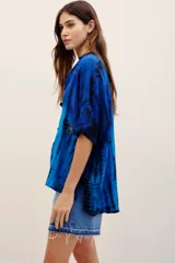 Camisa de viscosa con estampado tie-dye en tonos de azul y negro, de manga corta, cierre frontal con botones y bordados decorativos en el frente.