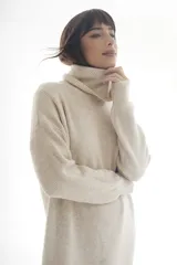 Vestido tipo sweater color beige, de tejido de punto acanalado, corte recto, largo a la rodilla y cuello alto.
