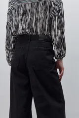 Jean wide leg negro de tiro alto, confeccionado en denim rígido, con diseño de cinco bolsillos, presillas para cinto, cierre frontal con botón y ruedo desflecado.