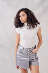 Top sin mangas, cuello tortuga, color blanco con acabado brillante o metálico. Tejido acanalado y ajustado al cuerpo.