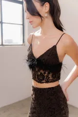 Top corto de encaje negro con breteles finos y detalle de plumas desmontables en el escote. Presenta un diseño ajustado al cuerpo con forro interior.