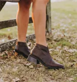 Bota corta de cuero vacuno con acabado metalizado y textura de reptil. Presenta punta fina, cierre lateral interno y taco cuadrado de madera.