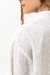 Vestido corto de broderie color crudo, con cuello camisero, cierre frontal parcial con botones, mangas tres cuartos acampanadas y corte evasé con volados.
