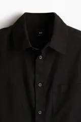 Camisa negra de manga larga con cuello clásico, tapeta con botones y bolsillo en el pecho. Corte regular.