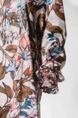 Vestido corto blanco con estampado floral en tonos marrones, azules y rosas, escote en V y mangas largas con puños elásticos.